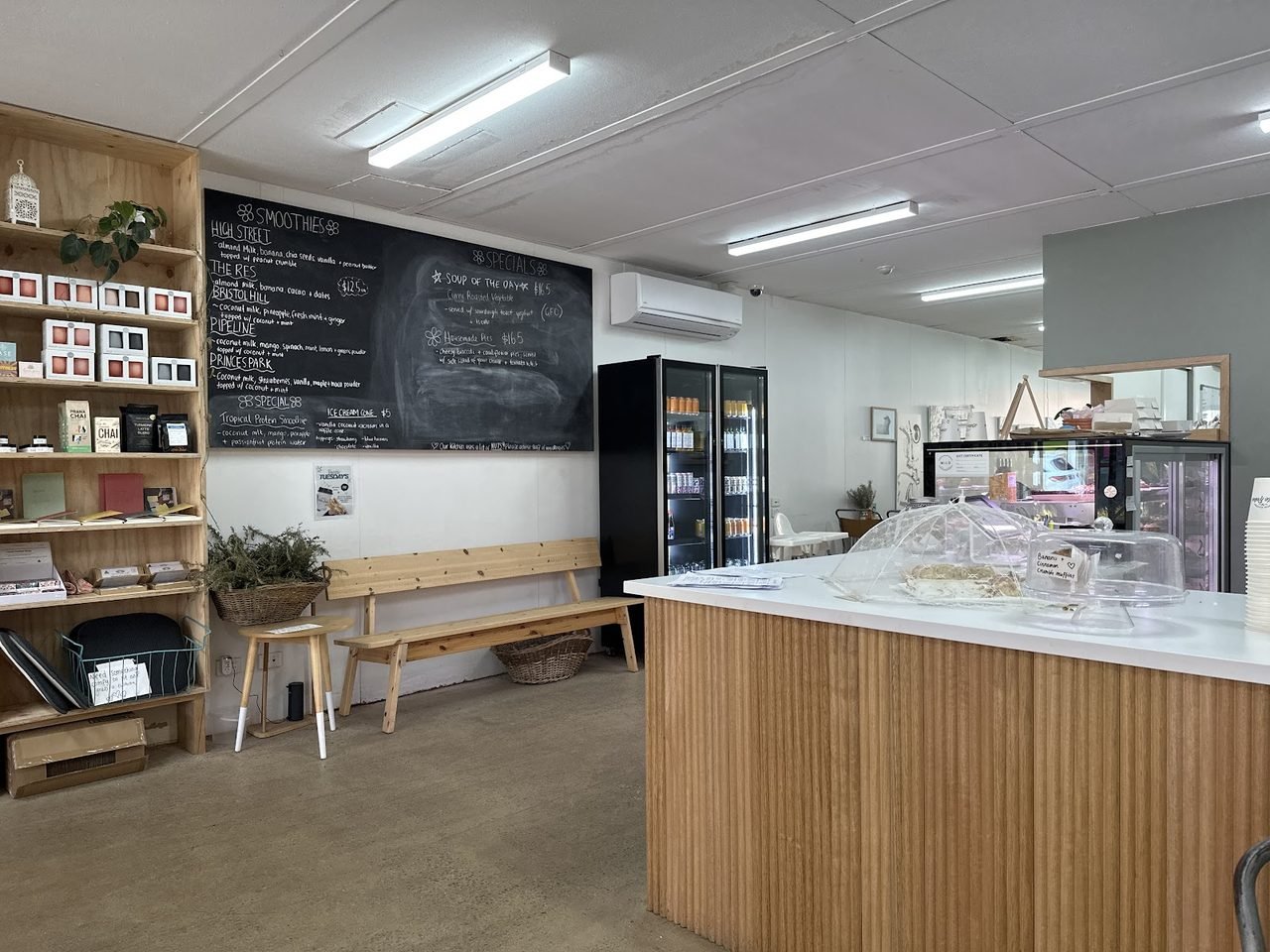 Inside Milo Cafe and Store: timber service counter, chalkboard menu, retail shelves and a cake dome.