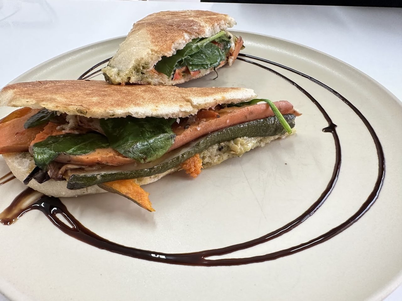 Grilled vegan panini stacked with roasted vegetables and greens on a stone plate with a balsamic swirl.